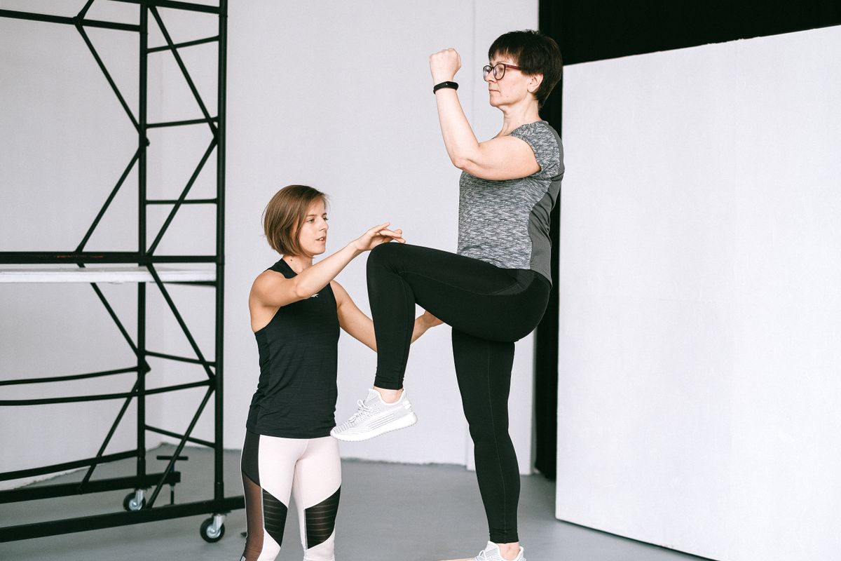 Older woman practising a knee lift with a fitness coach.